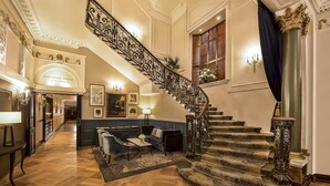 A grand staircase with ornate railings, a plush sofa, and a chandelier in a luxurious lobby. - The Bailey's Hotel London Kensington (London)