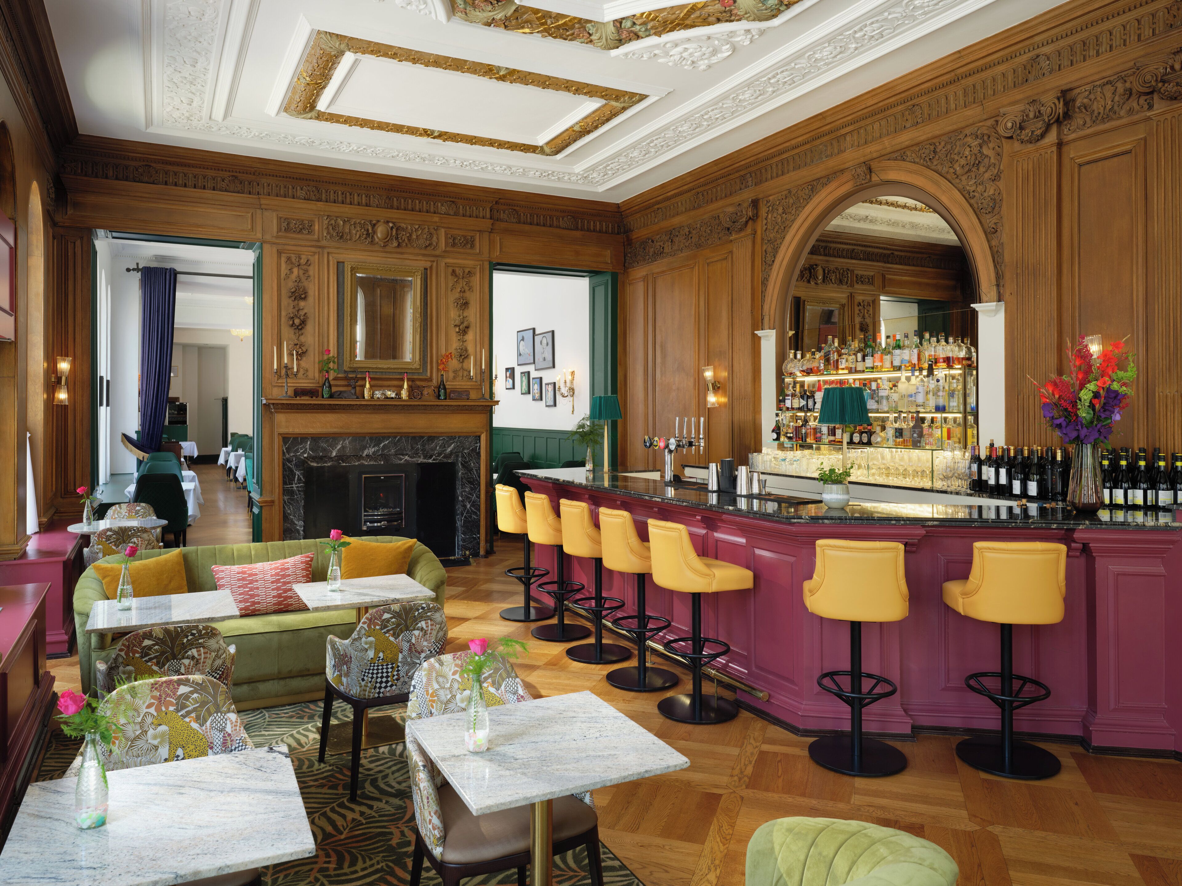 A bar area with a marble countertop, multiple bar stools, and a wine display. There is a fireplace with a mantel and a green upholstered sofa.