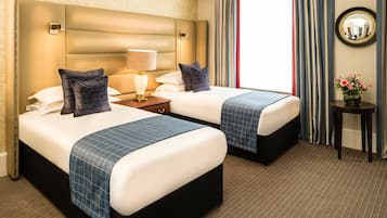 A hotel room with two beds, a nightstand with a lamp, a small table with a vase of flowers, and a large mirror on the wall.