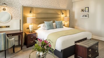 A hotel room with a large bed, bedside lamps, a desk, and a small side table with a vase of flowers.