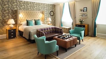 A bedroom with a tufted headboard, a bed with a plaid bedspread, two teal armchairs, a wooden coffee table, and a nightstand with a lamp.