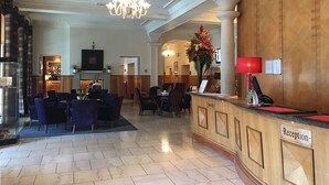 A hotel lobby with a reception desk, seating area, and a chandelier.
