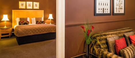A hotel room with a bed, bedside lamps, a nightstand, a sofa, a vase with flowers, and two framed pictures on the wall.