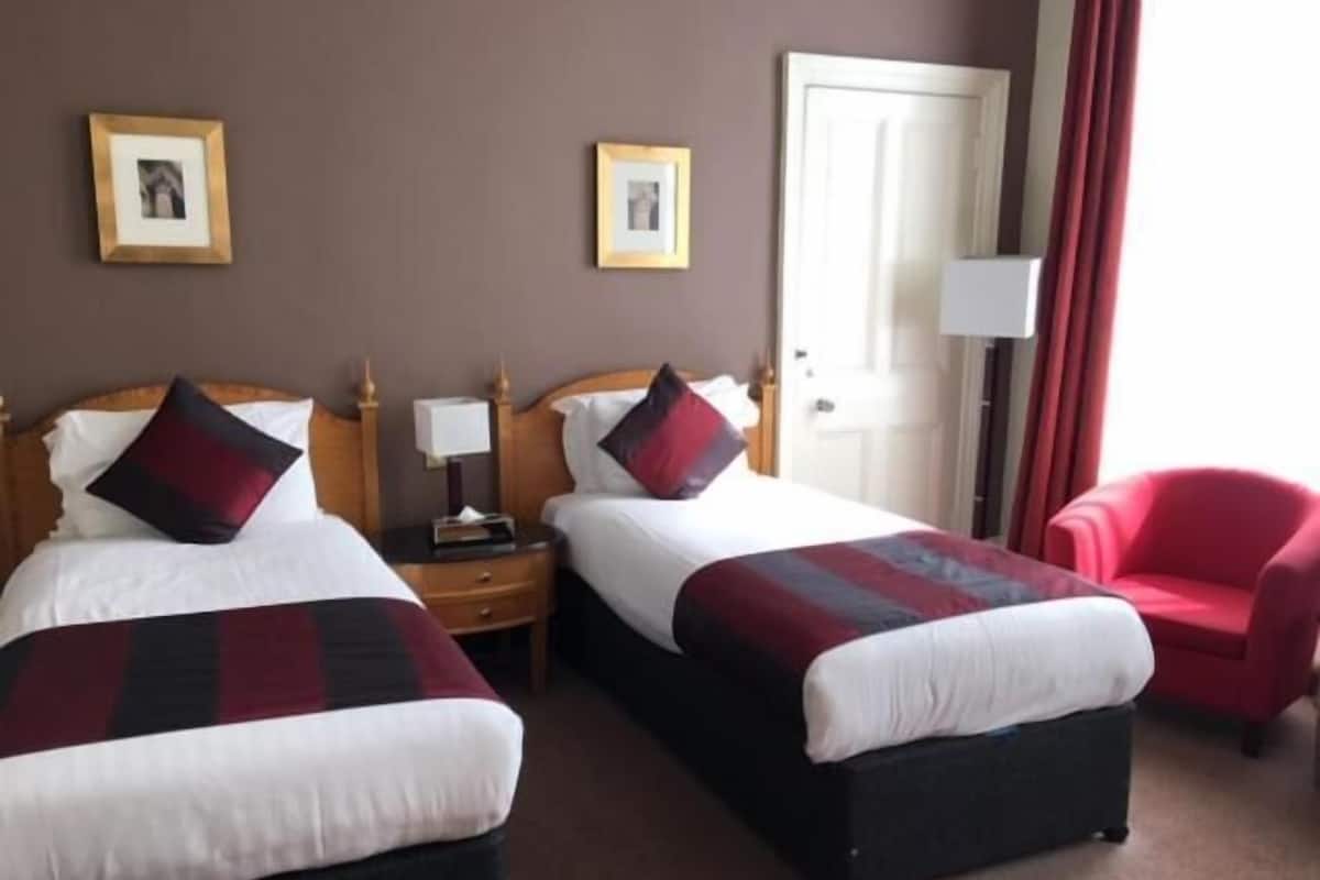 A hotel room with two beds, a red chair, and a door.
