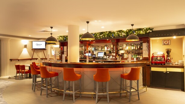 A bar area with a circular bar, orange bar stools, and a television screen displaying 'Caphorne'. - Copthorne Hotel Aberdeen (Aberdeen)
