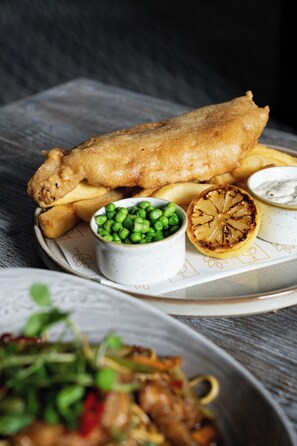 A plate of fish and chips with peas and lemon slices.