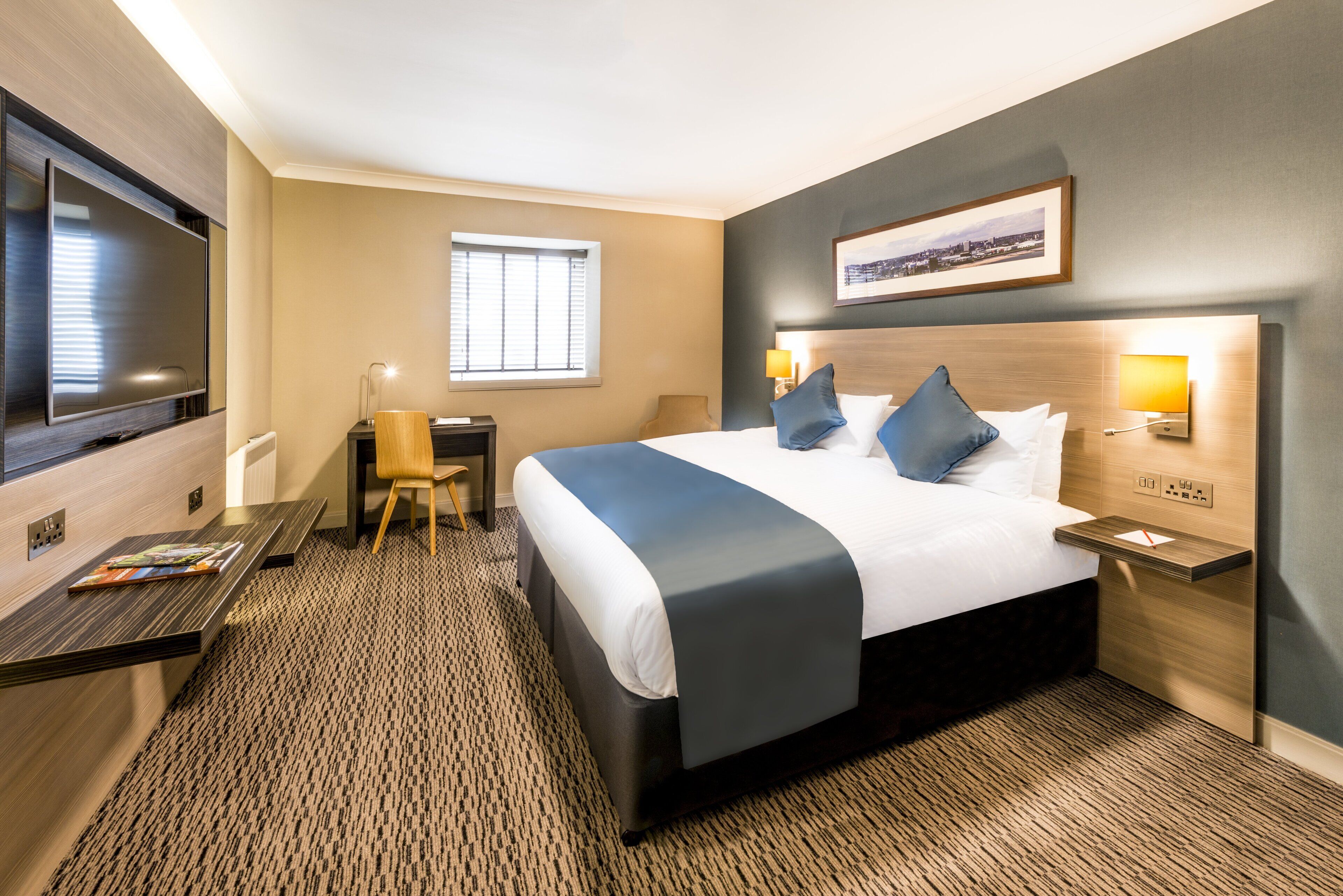 Une chambre d’hôtel avec un grand lit, des tables de chevet, un bureau, une chaise, une télévision et une fenêtre.