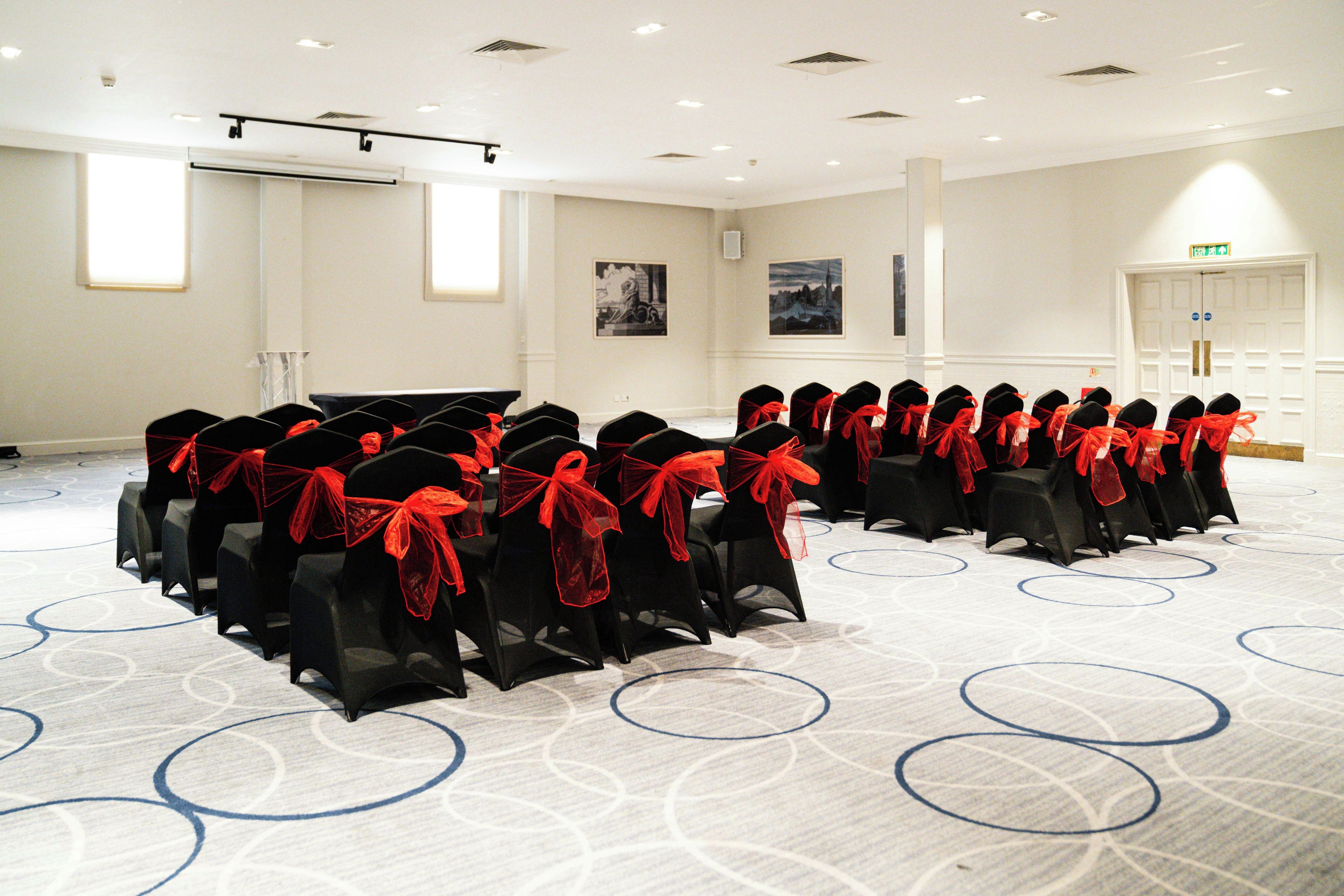 A conference room with rows of chairs, a projector screen, and a door with an exit sign.