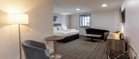 A hotel room with a bed, a desk, a chair, a lamp, and a window.