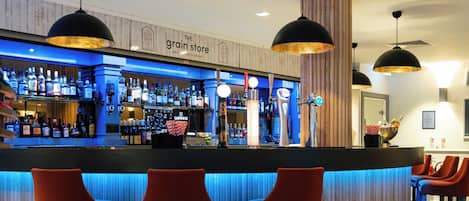 Zona bar con bancone, sgabelli e un cartello che riporta la scritta 'The Grain Store'.