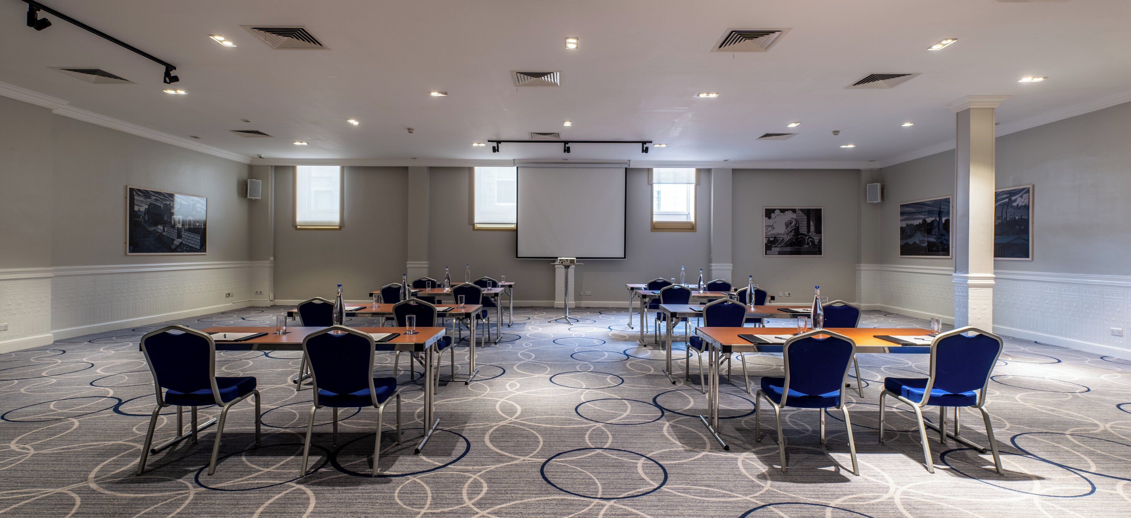 A conference room with a large screen, multiple tables, and chairs arranged for meetings.