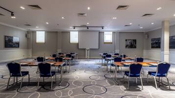 A conference room with a large screen, multiple tables, and chairs arranged for meetings.