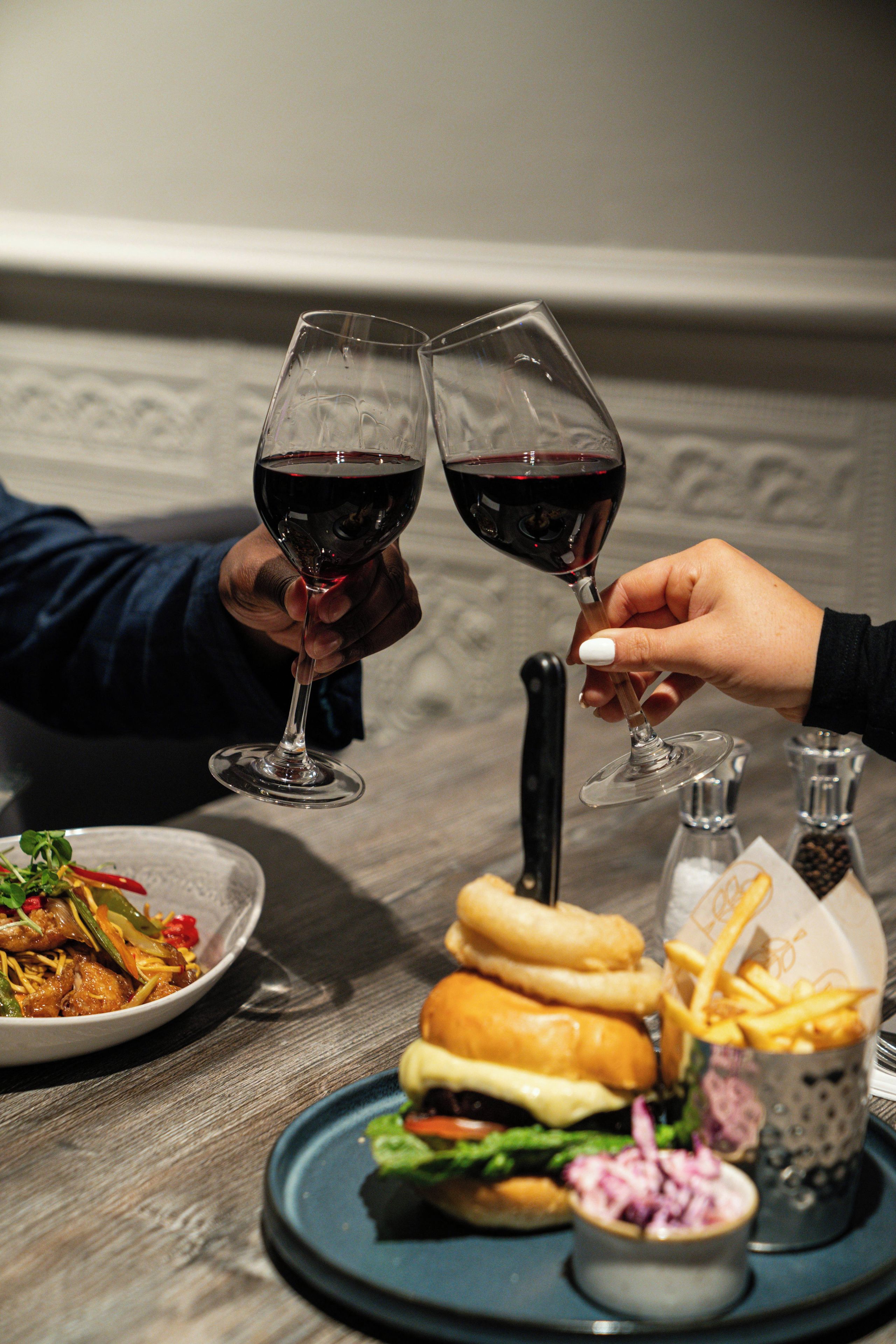 A dining table with a meal consisting of a burger, fries, and a salad, along with two wine glasses filled with red wine.