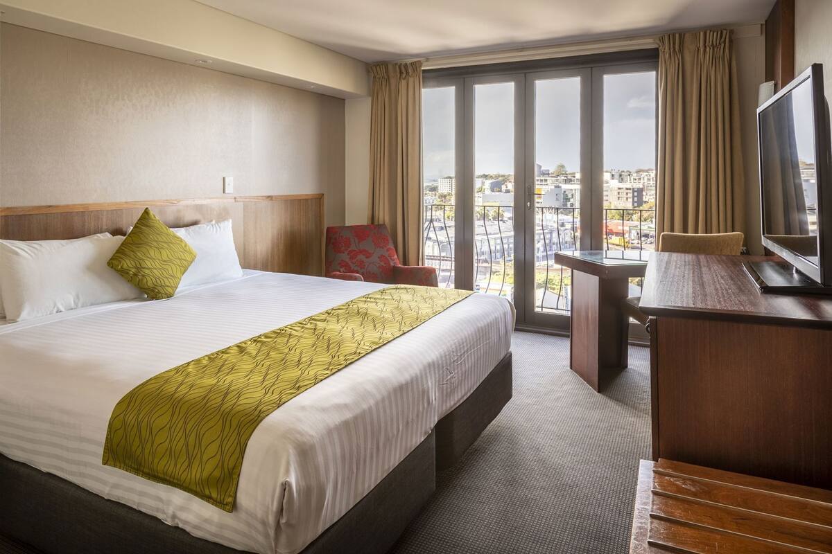A hotel room with a large bed, a desk, a chair, and a TV.