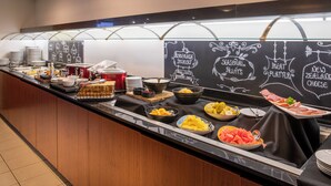 Un bufé con diversos alimentos y un menú en pizarra que ofrece opciones como yogur casero, frutas de temporada, tabla de carnes y queso de Nueva Zelanda.