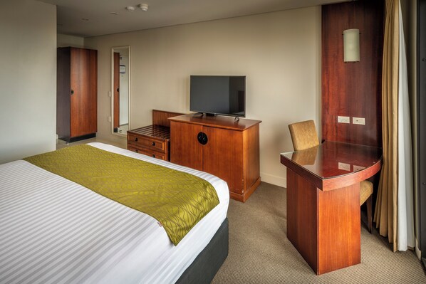 A hotel room with a bed, a wooden desk, a television, and a chair.