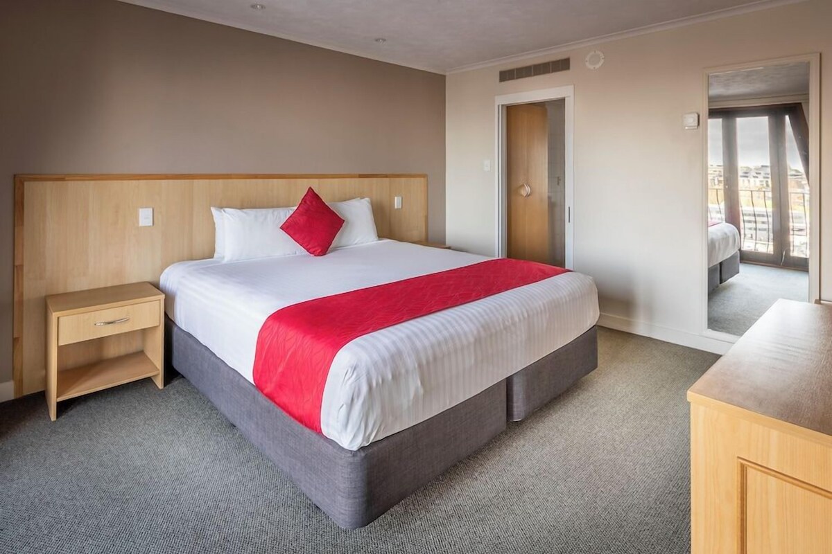 Une chambre d’hôtel comprenant un lit, une table de chevet, une armoire et une porte donnant sur un balcon.