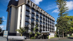 Un hotel de varios pisos con un diseño arquitectónico moderno, que cuenta con balcones, una entrada destacada y un cielo despejado.