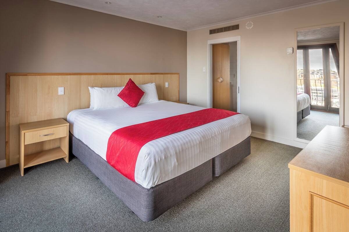 A hotel room with a bed, a nightstand, a dresser, and a door leading to a balcony.