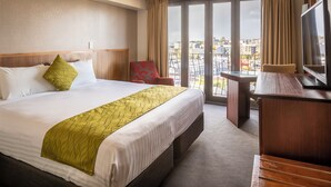 Habitación de hotel con una cama grande, un escritorio, un televisor y un balcón con vista a la ciudad.