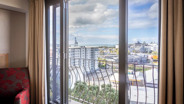 Una habitación con un ventanal grande, un sofá estampado y vista a un paisaje urbano con edificios y un puente.