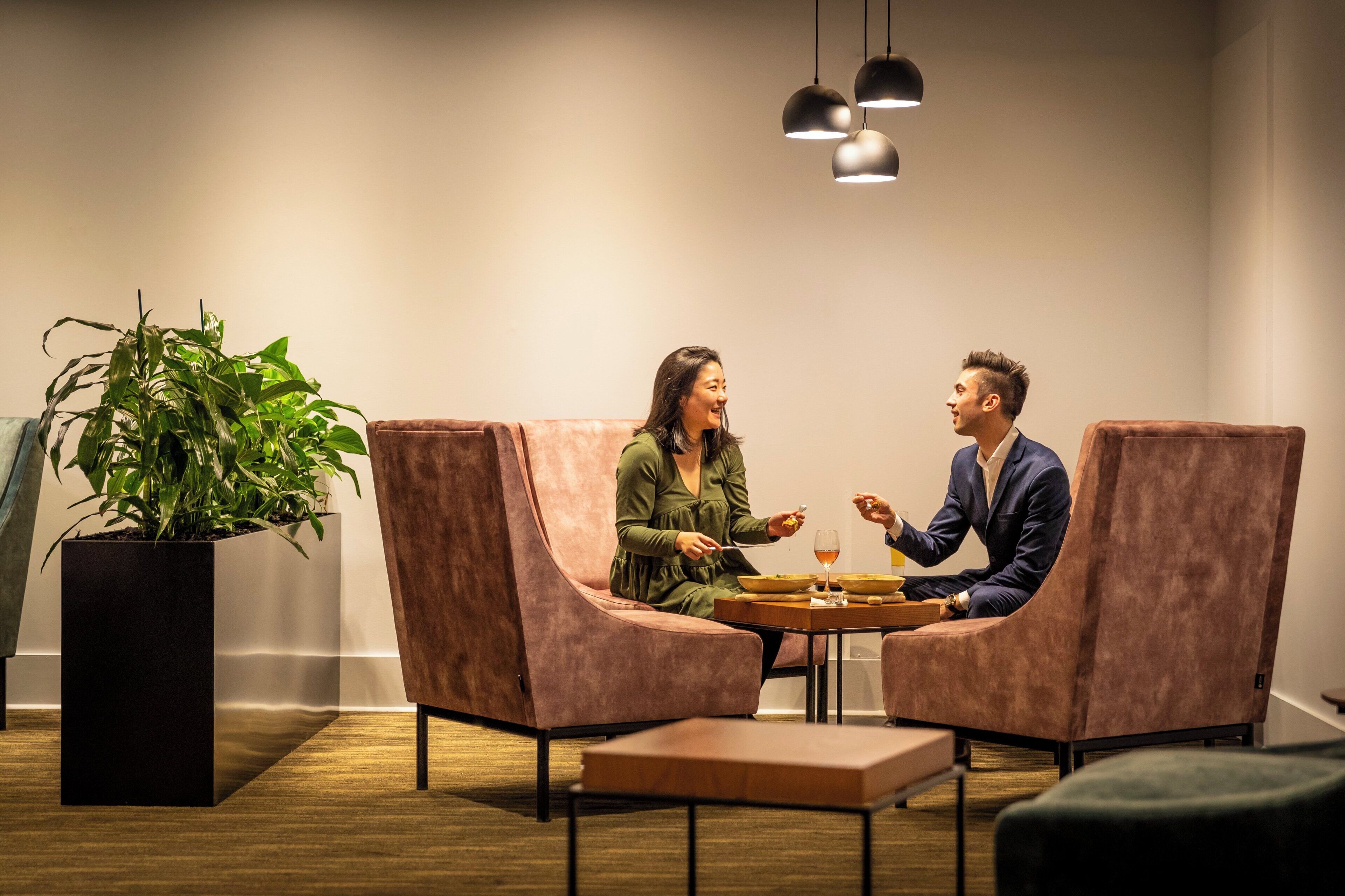 Un interior moderno con dos sillones acolchados enfrentados alrededor de una pequeña mesa, una planta en maceta e iluminación colgante.