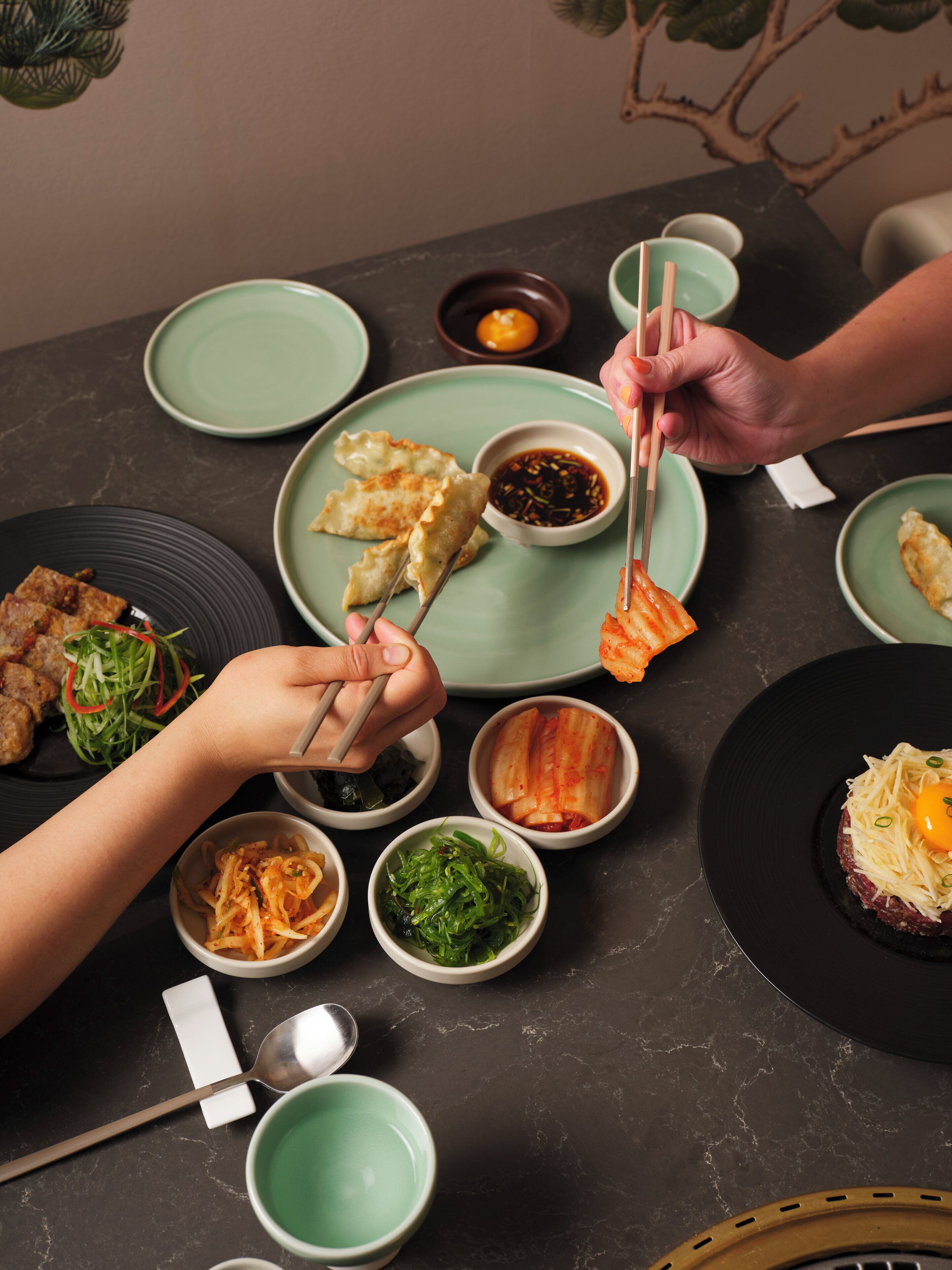 A table set with various dishes, including dumplings, kimchi, and a dish with shredded meat and an egg.