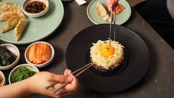 A dining table with various dishes, including a plate with a raw egg yolk on top of a meat patty, surrounded by side dishes and condiments.
