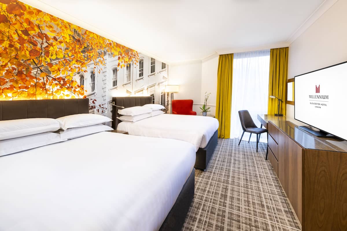 Habitación de hotel con dos camas, un escritorio, un televisor y un ventanal con cortinas.