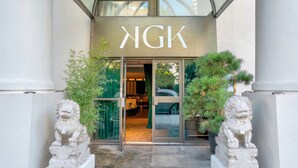 Ein Gebäudeeingang mit dem Schild "NGK" über den Türen, flankiert von zwei steinernen Löwenstatuen.