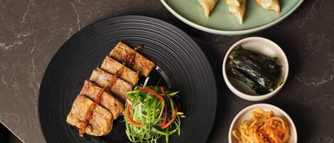 A table with various dishes, including dumplings and a salad, accompanied by dipping sauces and seaweed.