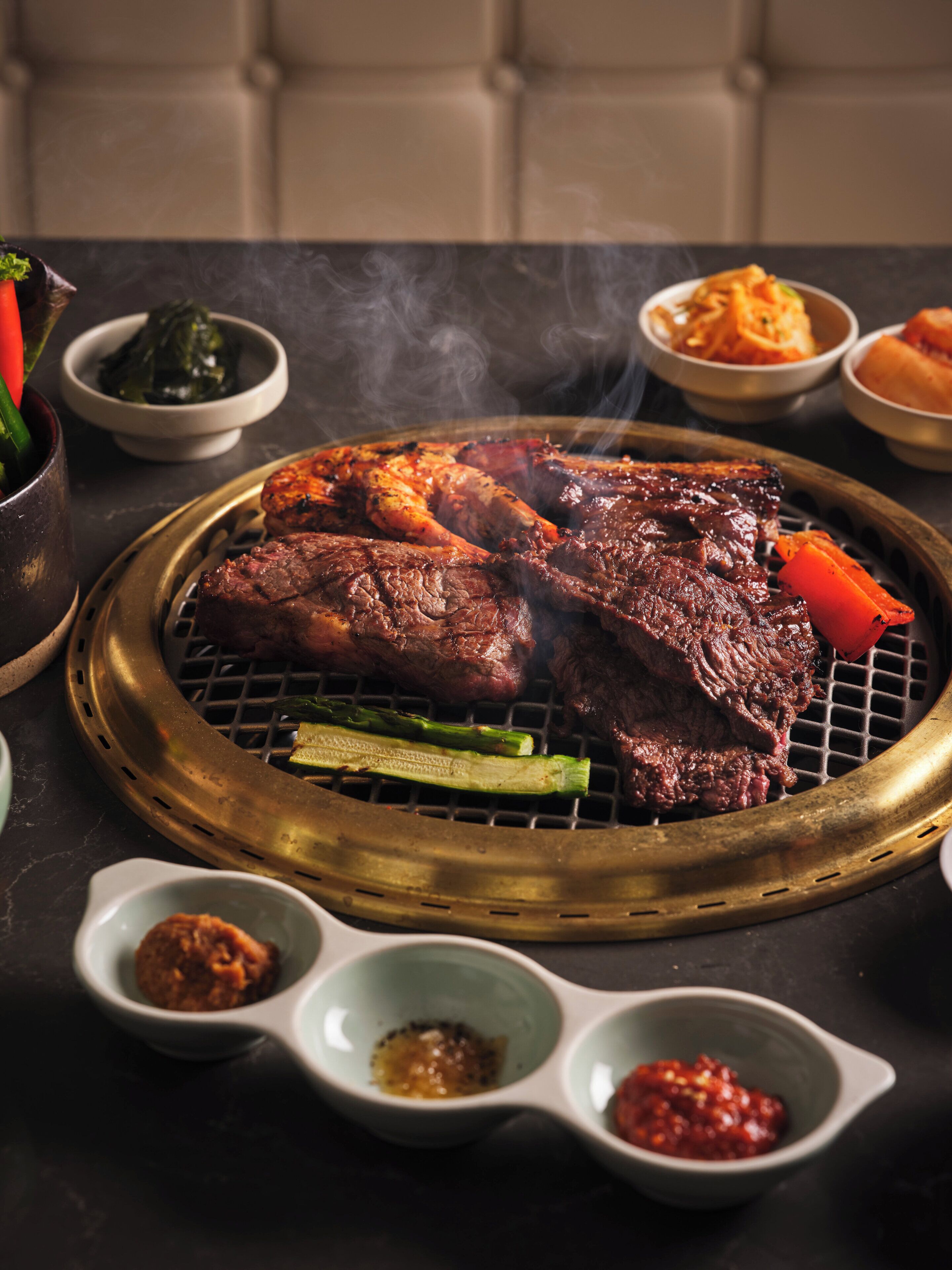 A grill with meat and vegetables, accompanied by small bowls of sauces.