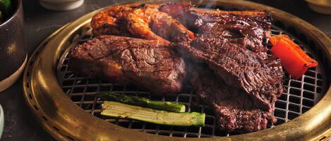 A grill with meat and vegetables, accompanied by small bowls of sauces.