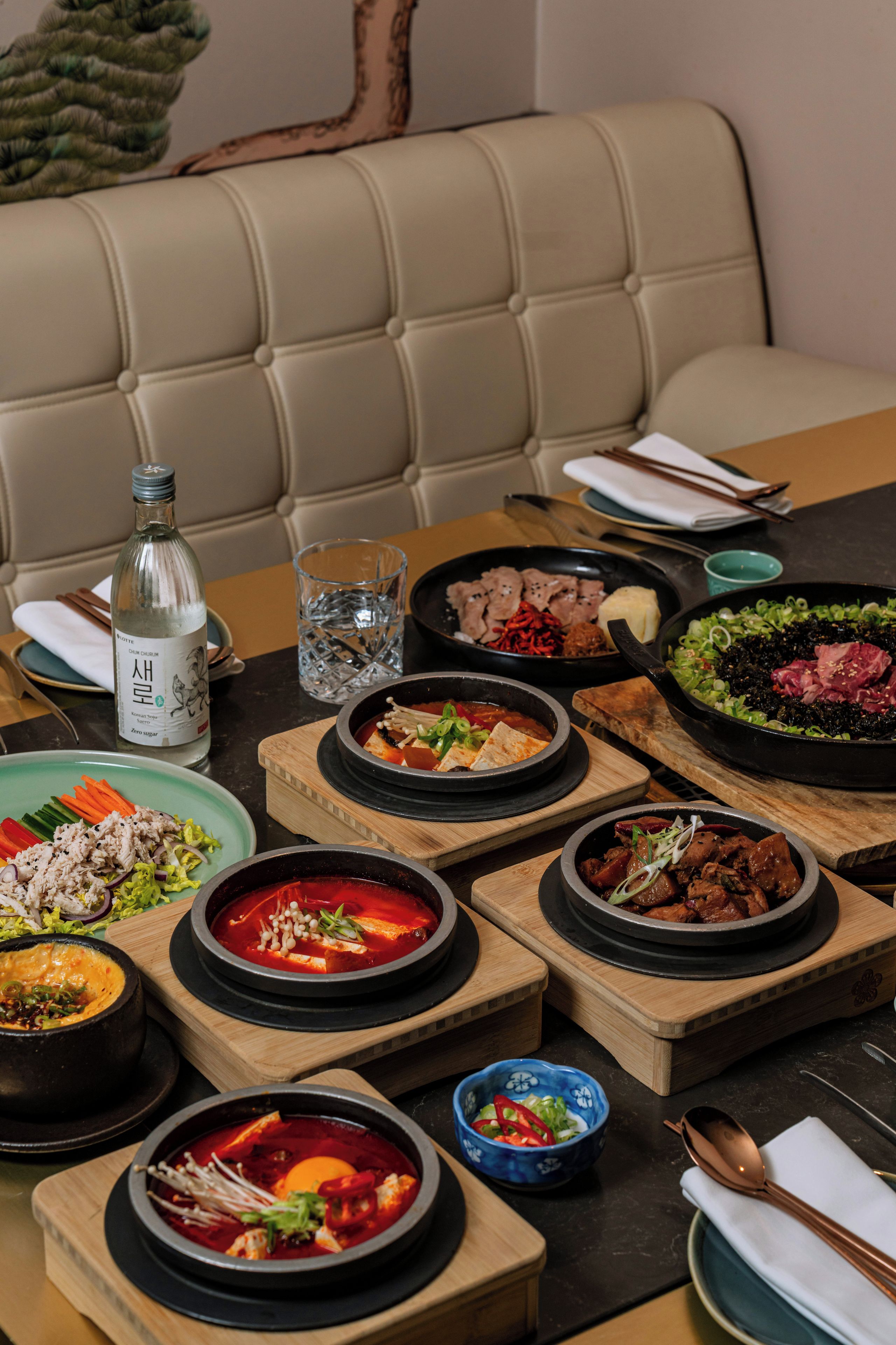 A table set with various Korean dishes, a bottle of liquor, and a glass of water.