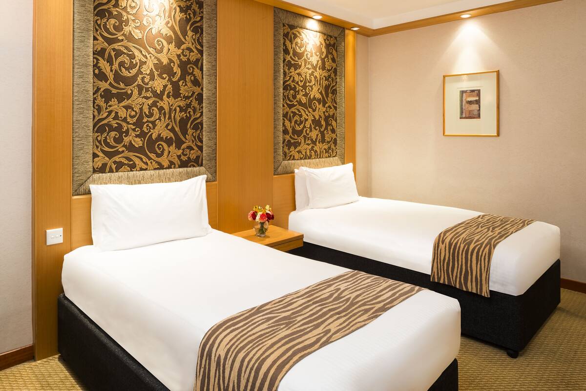 Habitación de hotel con dos camas, una mesita de noche con un florero y un cuadro en la pared.