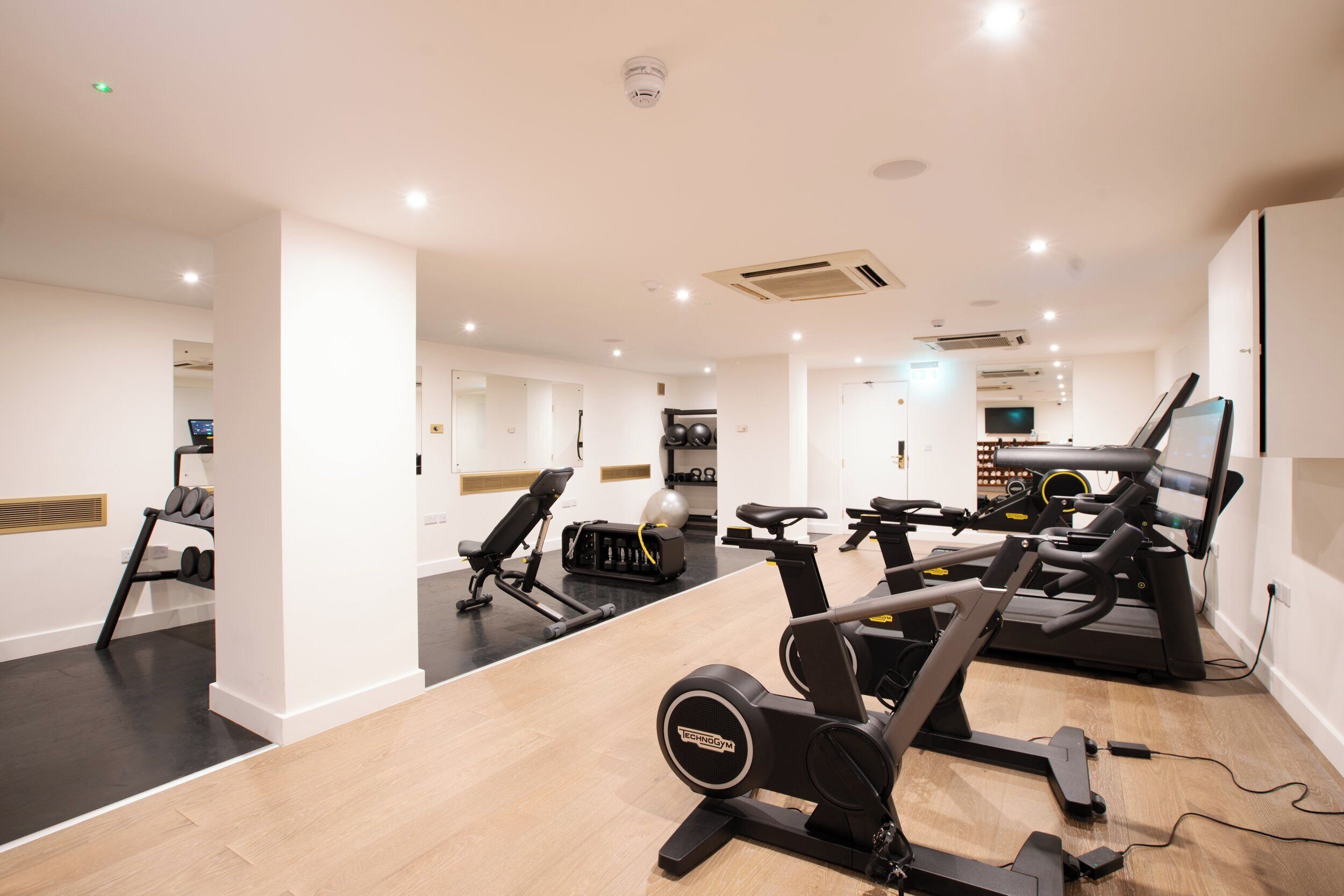 Une salle de sport moderne équipée de machines de cardio, de bancs de musculation et d’un mur recouvert de miroirs.
