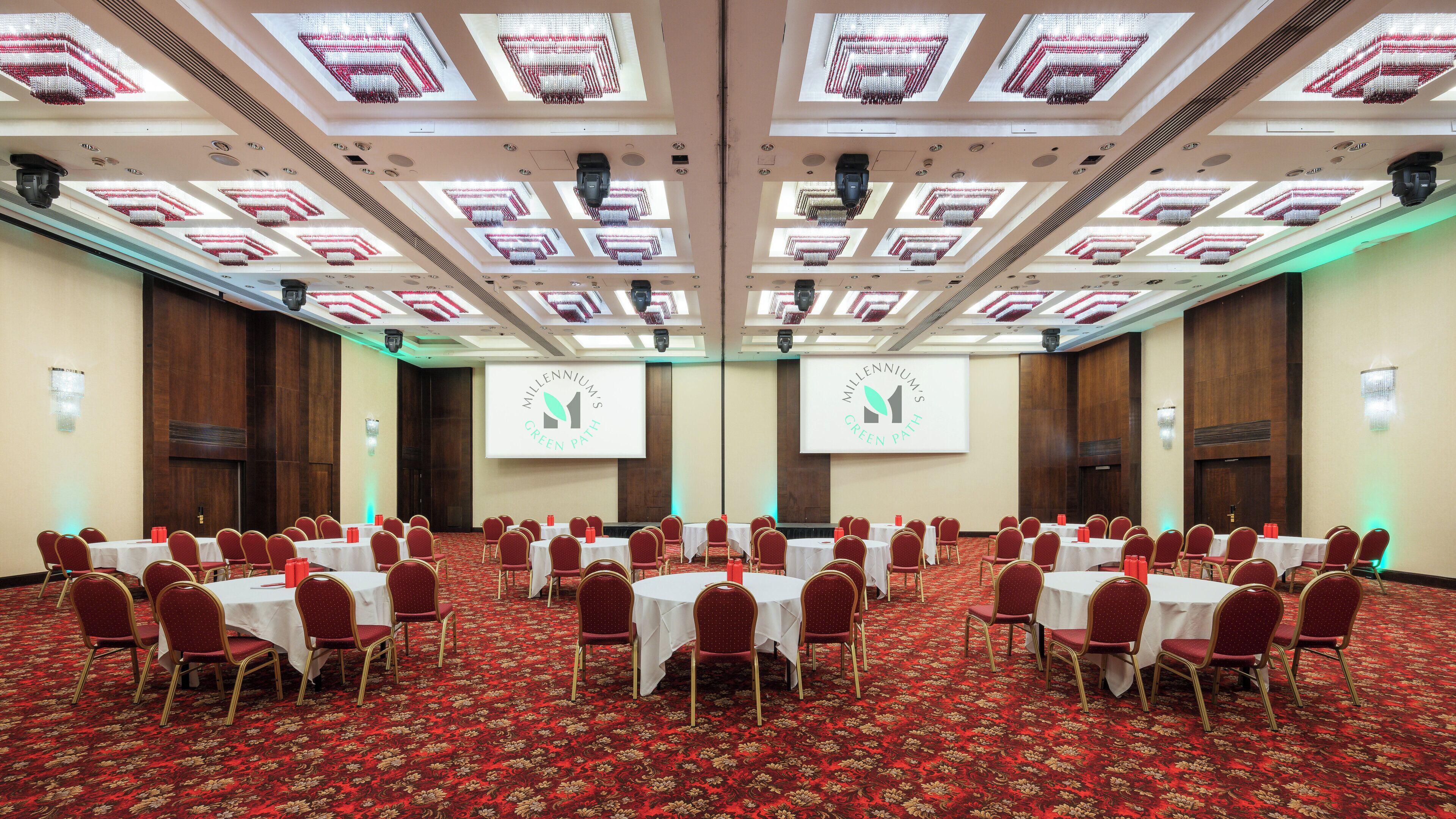 Une salle de conférence dotée de plusieurs tables et chaises, d’un tapis rouge et d’un plafond orné de luminaires carrés.