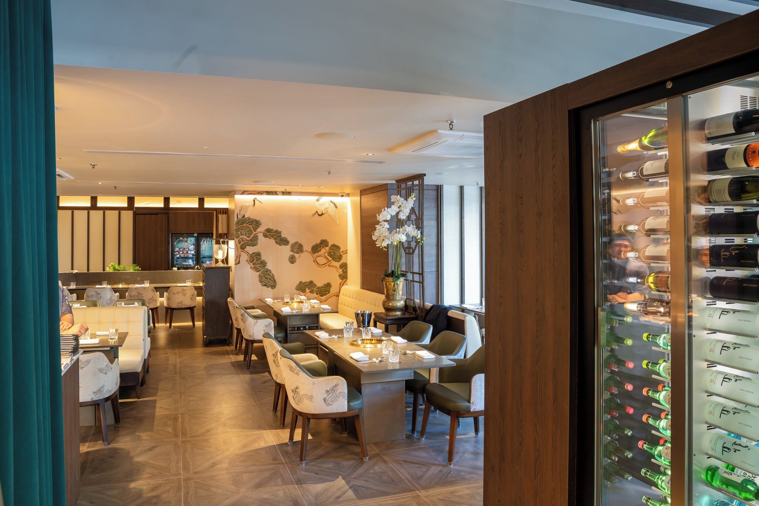 A modern restaurant with a long dining table, comfortable seating, and a wine refrigerator.