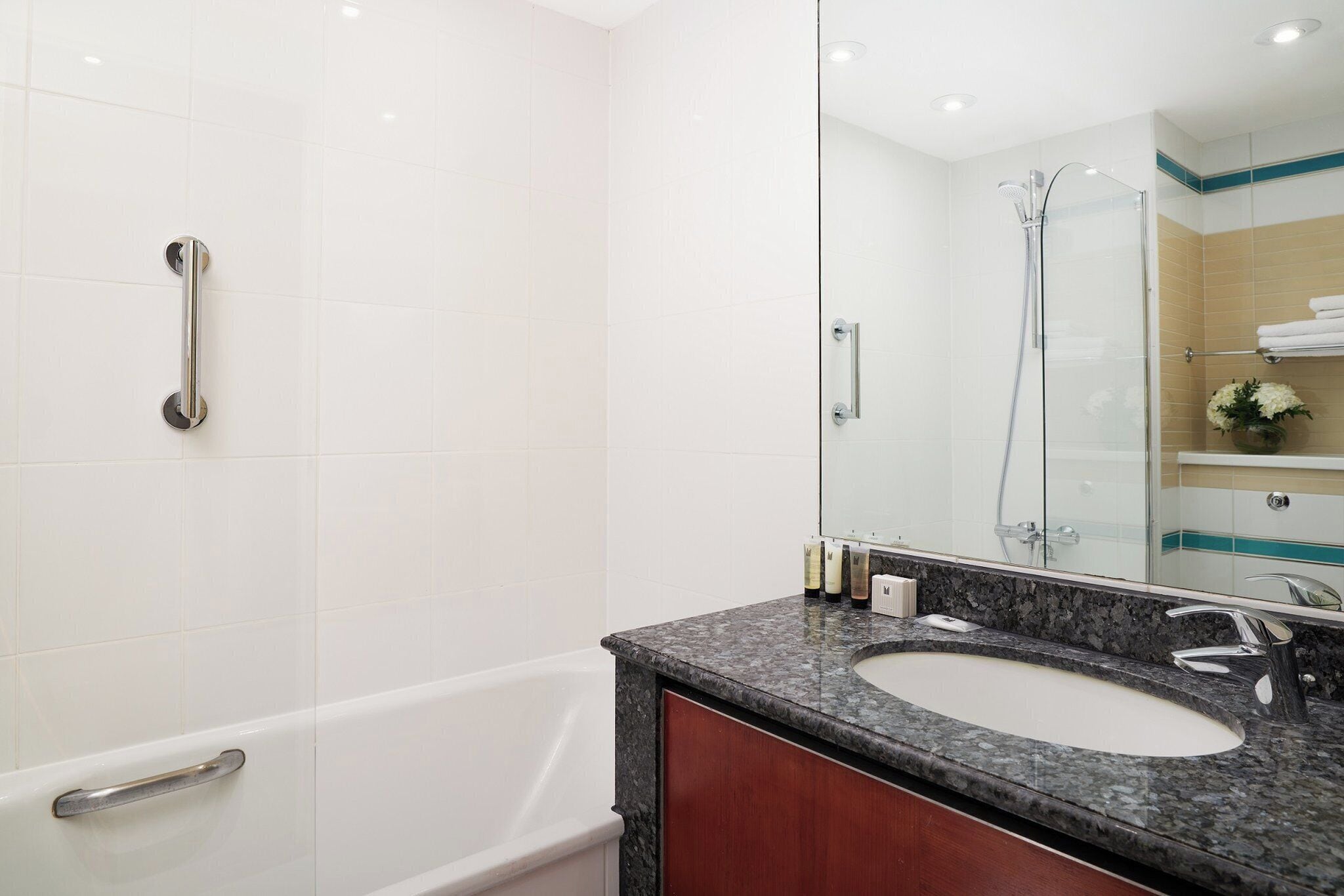 Un baño moderno con una bañera blanca, un lavamanos de encimera de granito y una mampara de vidrio.