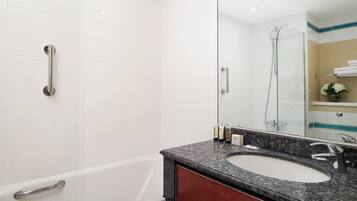 Un baño moderno con una bañera blanca, un lavamanos de encimera de granito y una mampara de vidrio.