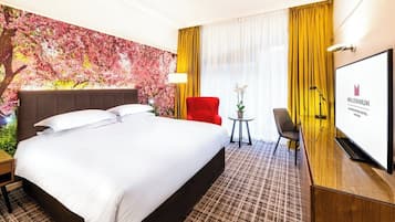 Ein Hotelzimmer mit einem großen Bett, einem roten Sessel, einem kleinen runden Tisch mit Lampe und einem Fernseher auf einer Holzkommode.