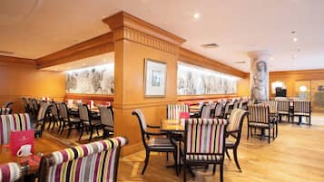 A restaurant with striped upholstered chairs, wooden tables, and a marble column.