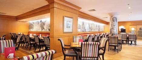 A restaurant with striped upholstered chairs, wooden tables, and a marble column.