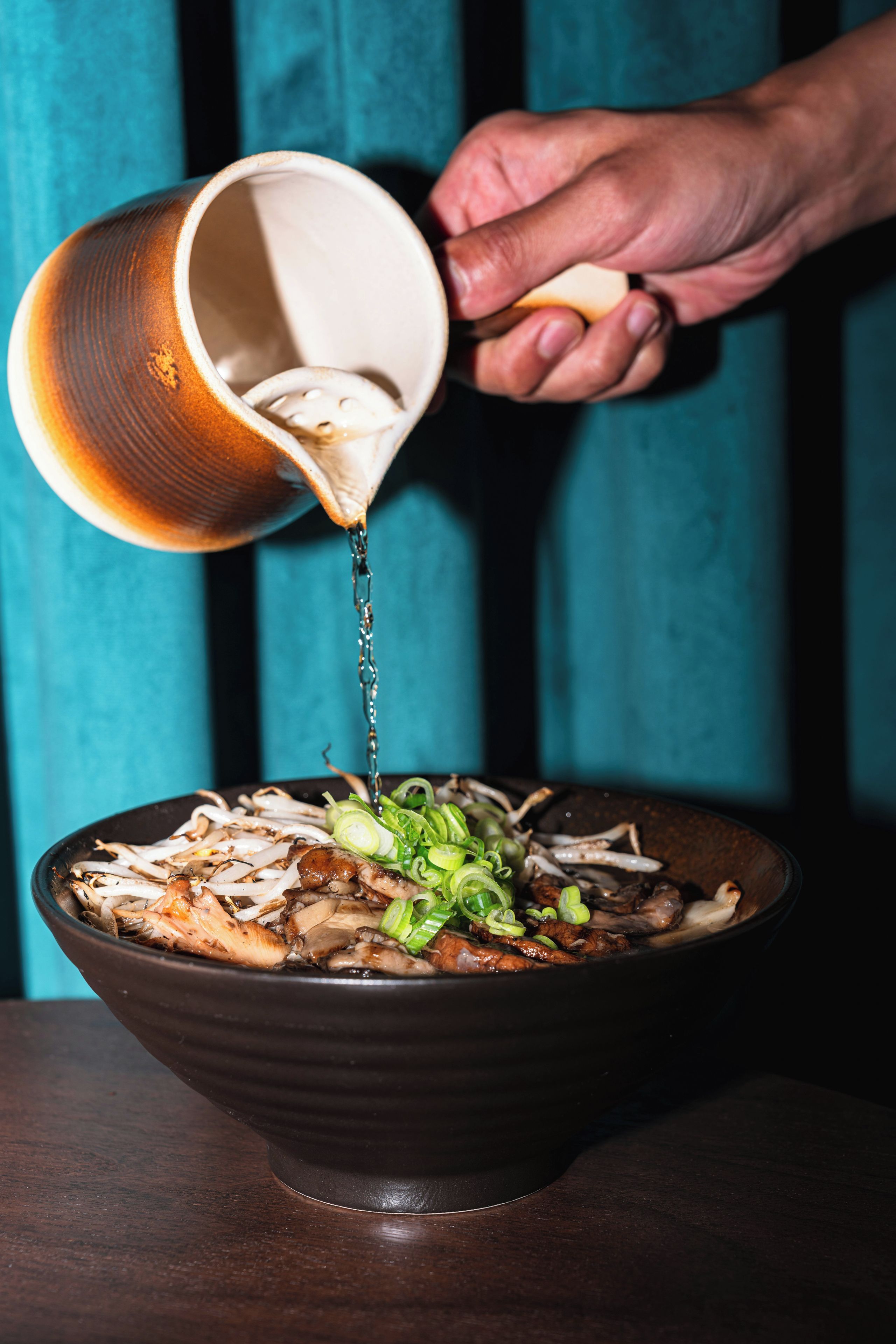 A hand pouring a liquid from a cup into a bowl containing food.