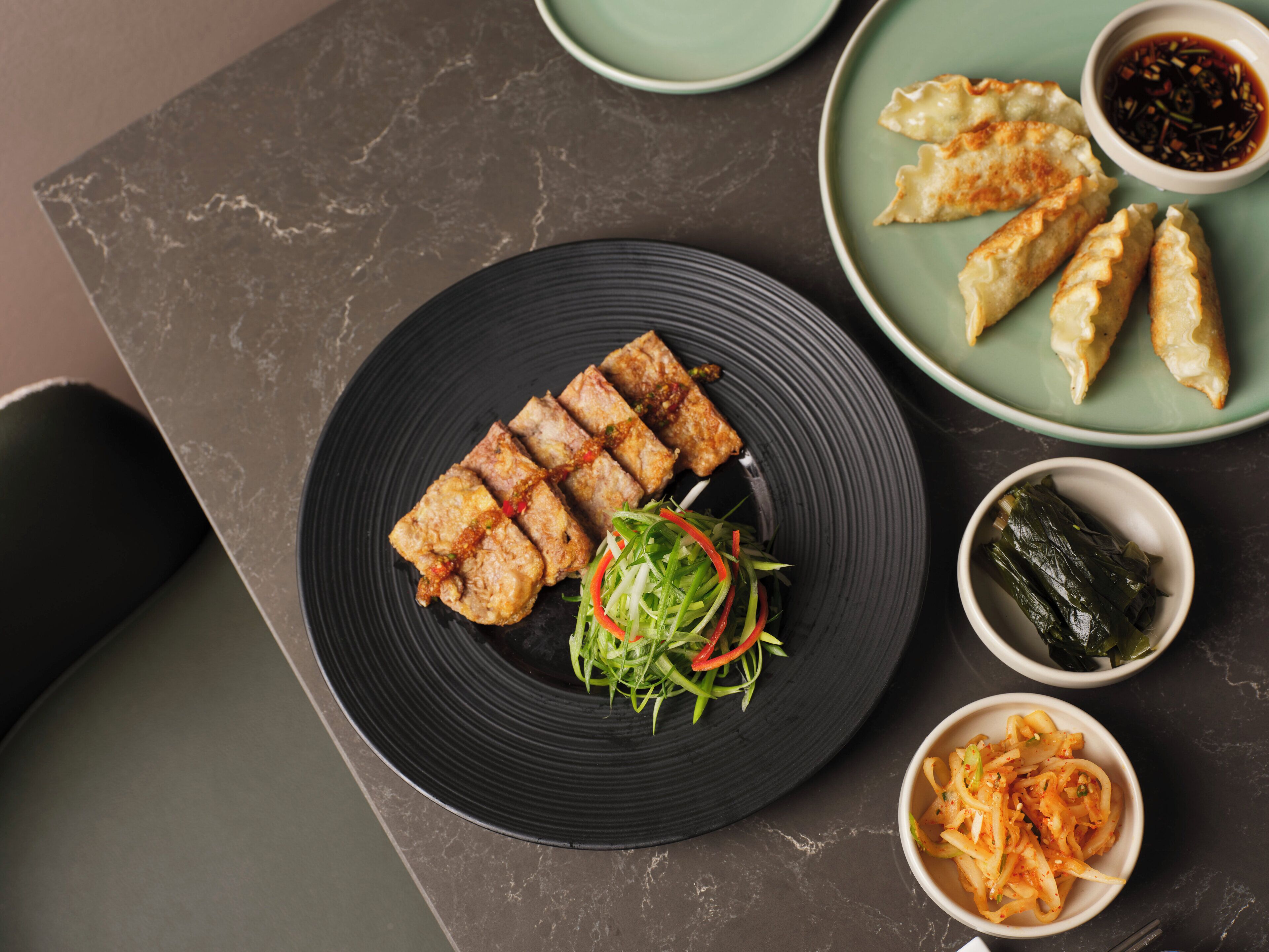A plate of food with various dishes including dumplings, a salad, and a bowl of noodles.