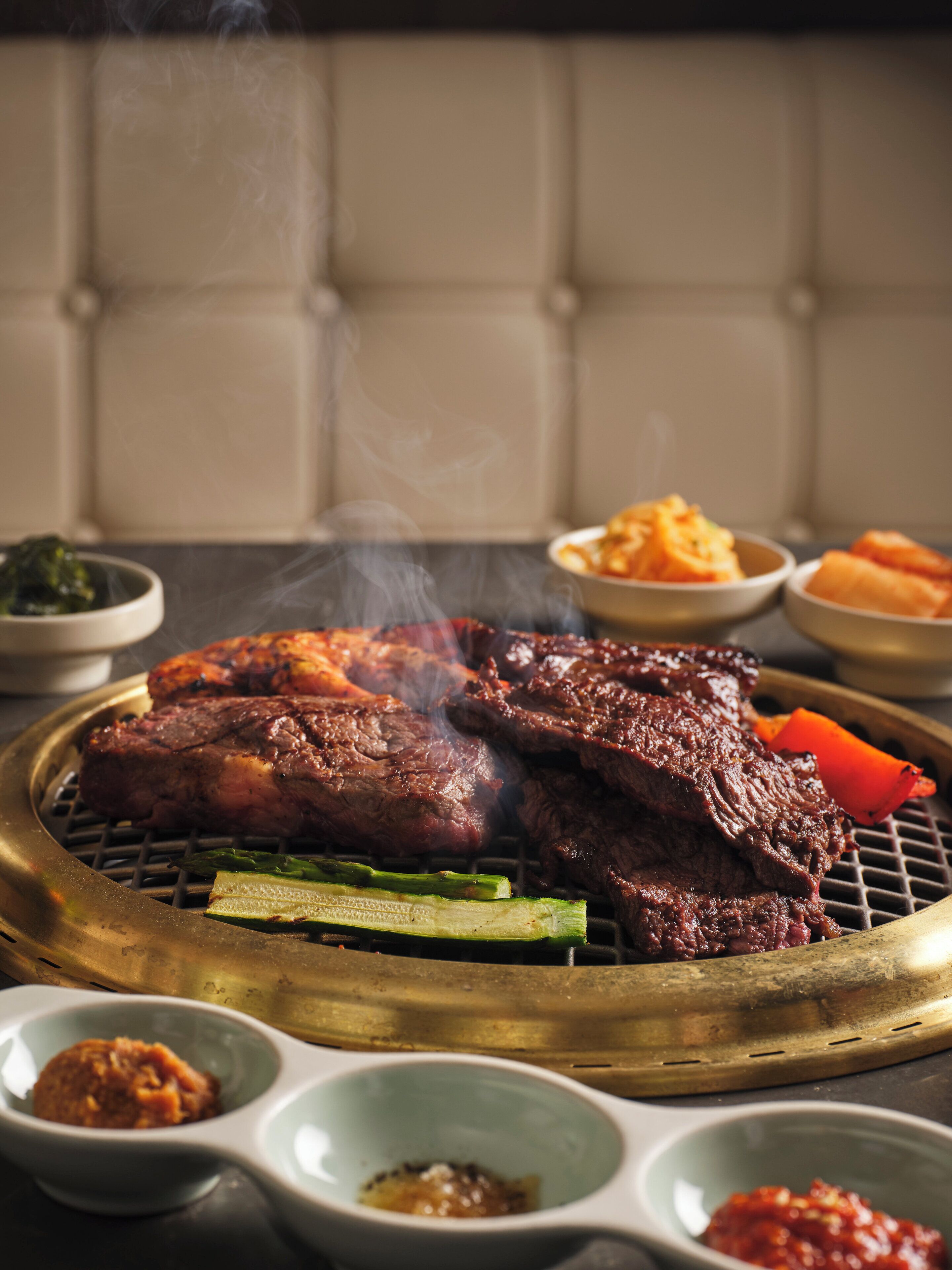 Ein Grill mit verschiedenen Fleischstücken und Gemüsesorten, dazu kleine Schalen mit Soßen.
