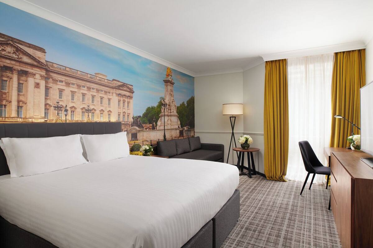 Una habitación de hotel con una cama grande, un sofá, un escritorio y un mural de un edificio histórico.