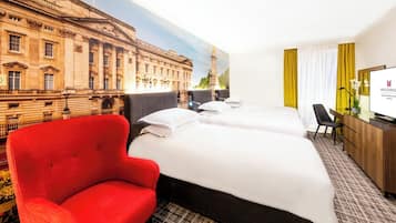 Habitación de hotel con dos camas, un sillón rojo, un escritorio con computadora y un ventanal con cortinas.