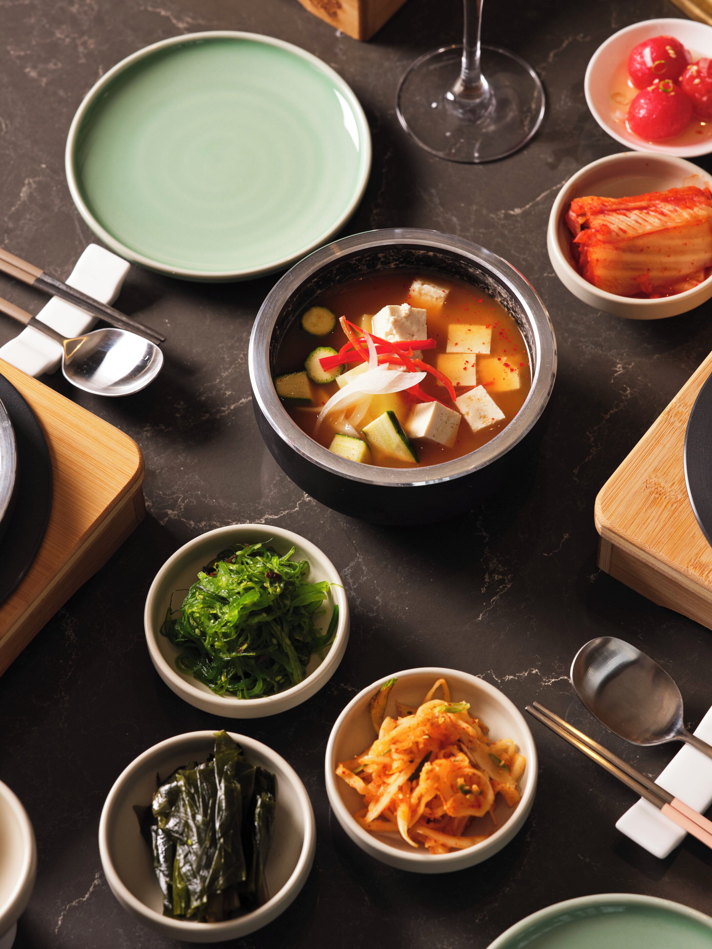 A table with various dishes including a bowl of soup, kimchi, and vegetables.