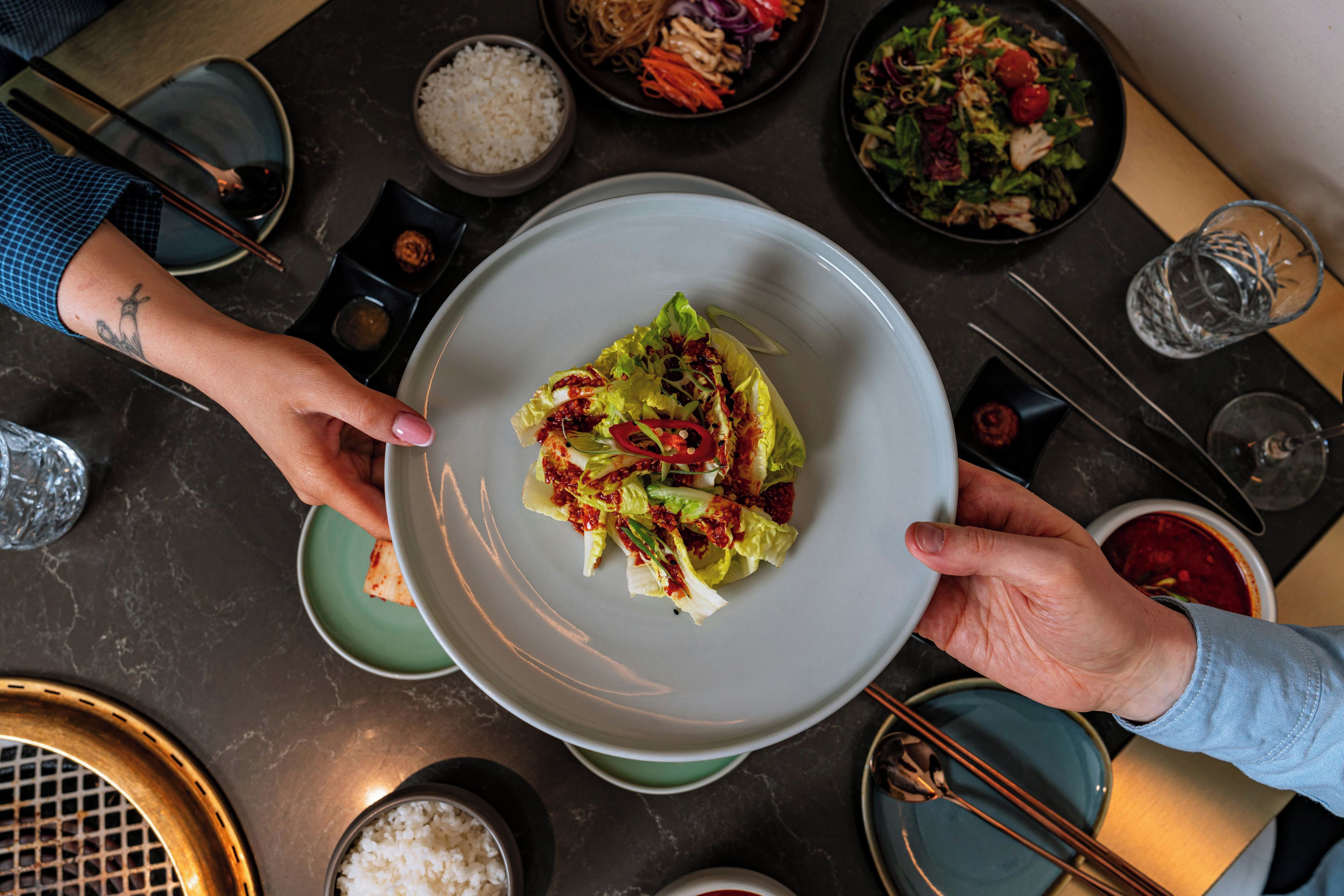 Una mesa de comedor con varios platos, incluyendo una ensalada y arroz, y una persona sosteniendo un tazón.